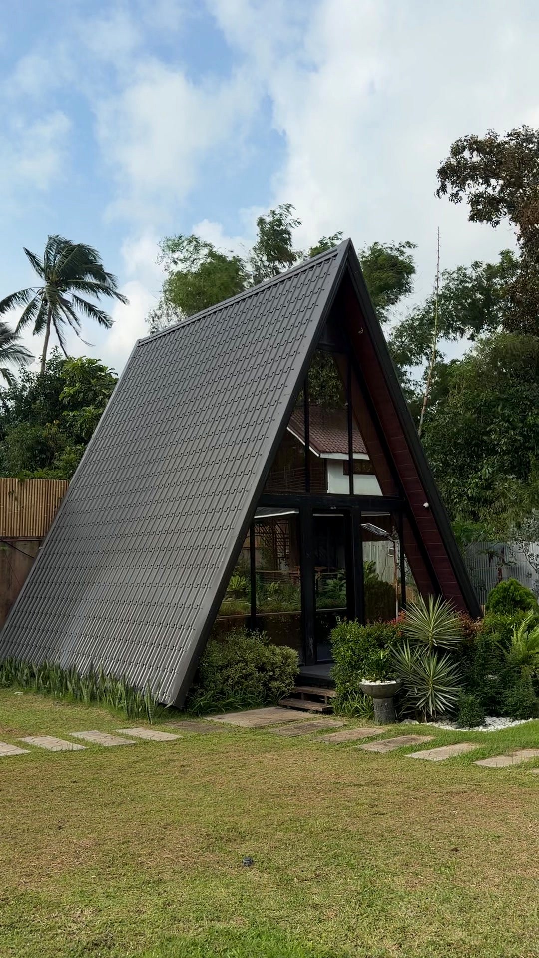 A-Frame Villa exterior — dramatic steep dark shingled roof with a glass front, surrounded by palm trees