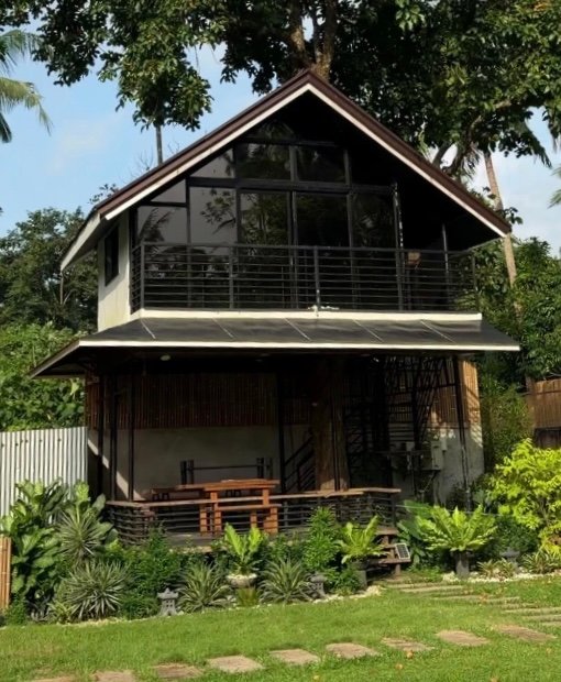 Two-story Treehouse villa with dark wood cladding, tucked beneath a large tree